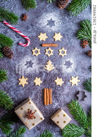 Christmas sweets and cookies in form of christmas tree placed on gray desk with pine cone and branch on the side. Winter and christmas decorations, cinnamon, sugar and star anise. 136149982