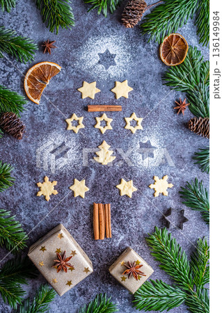 Christmas sweets and cookies in form of christmas tree placed on gray desk with pine cone and branch on the side. Winter and christmas decorations, cinnamon, sugar and star anise. 136149984