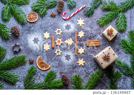 Christmas sweets and cookies in form of christmas tree placed on gray desk with pine cone and branch on the side. Winter and christmas decorations, cinnamon, sugar and star anise. 136149987