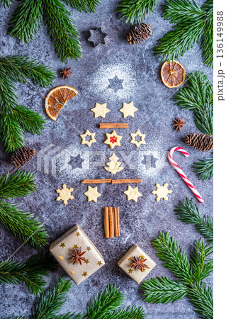 Christmas sweets and cookies in form of christmas tree placed on gray desk with pine cone and branch on the side. Winter and christmas decorations, cinnamon, sugar and star anise. Christmas sweets and cookies in form of christmas tree placed on gray desk with pine cone and branch on the side. Winter and christmas decorations, cinnamon, sugar and star anise. 136149988