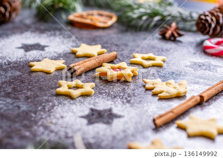 Christmas sweets and cookies in form of christmas tree placed on gray desk with pine cone and branch on the side. Winter and christmas decorations, cinnamon, sugar and star anise. 136149992