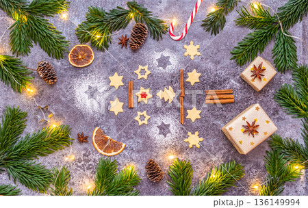 Christmas sweets and cookies in form of christmas tree placed on gray desk with pine cone and branch on the side. Winter and christmas decorations, small glowing light on the side 136149994