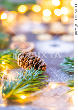Christmas sweets and cookies placed on gray desk. Winter decorations, pine tree and cone. Concept of christmas, gifts and holidays. Glowing lights in the background. Christmas sweets and cookies placed on gray desk. Winter decorations, pine tree and cone. Concept of christmas, gifts and holidays. Glowing lights in the background. 136150011
