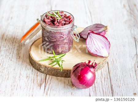 Red onion marmalade placed on wooden trunk with wood texture background. Jam from onion is delicious part of French cuisine. Homemade jam in transparent glass, vibrant colors, soft light. 136150120