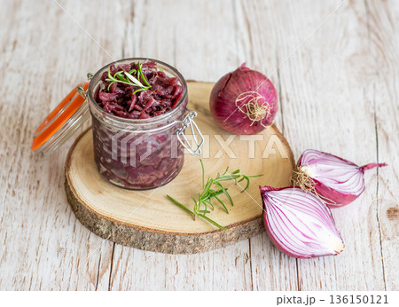 Red onion marmalade placed on wooden trunk with wood texture background. Jam from onion is delicious part of French cuisine. Homemade jam in transparent glass, vibrant colors, soft light. 136150121