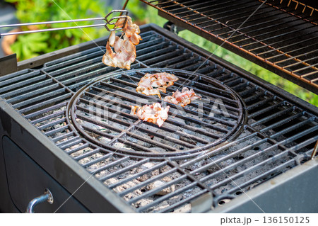 Bacon cooking on the hot grill, preparation of unhealthy food. 136150125