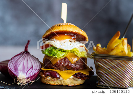 Homemade cheeseburger placed on wooden desk, with the onion and french fries on the side. Gray background. Homemade cheeseburger placed on wooden desk, with the onion and french fries on the side. Gray background. 136150136