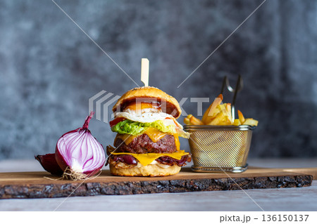Homemade cheeseburger placed on wooden desk, with the onion and french fries on the side. Gray background. 136150137