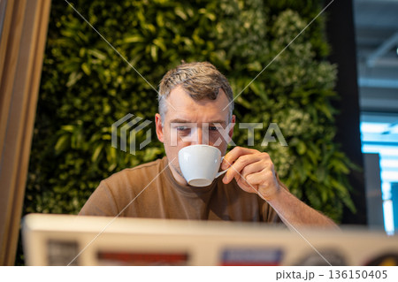 Man enjoying coffee while working on laptop Man enjoying coffee while working on laptop 136150405