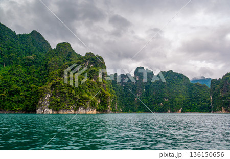 View of Khao Sok Lake in Krabi province, Thailand, with towering limestone cliffs covered in tropical rainforest rising above the calm surface of the lake. 136150656