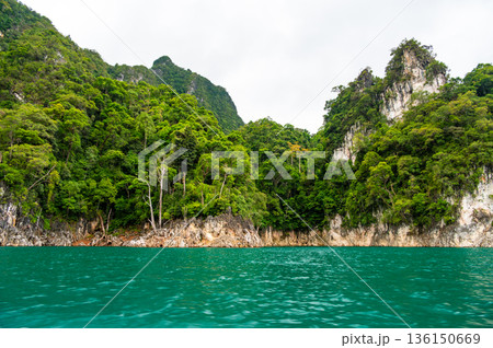 View of Khao Sok Lake in Krabi province, Thailand, with towering limestone cliffs covered in tropical rainforest rising above the calm surface of the lake. View of Khao Sok Lake in Krabi province, Thailand, with towering limestone cliffs covered in tropical rainforest rising above the calm surface of the lake. 136150669
