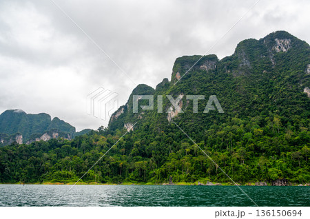 View of Khao Sok Lake in Krabi province, Thailand, with towering limestone cliffs covered in tropical rainforest rising above the calm surface of the lake. View of Khao Sok Lake in Krabi province, Thailand, with towering limestone cliffs covered in tropical rainforest rising above the calm surface of the lake. 136150694