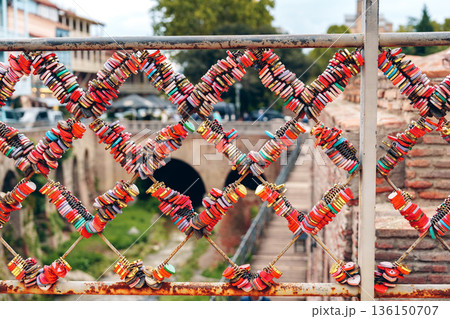 Visitors leave colorful locks on a fence near an old stone bridge in a city park 136150707