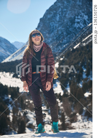 Woman tourist hiking in snow mountain, looking up with happy smile. Winter travel adventure in nature landscape. Outdoor activity. 136150726