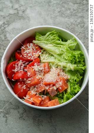 Fresh salad bowl with lettuce, tomatoes, and cheese on gray surface 136150737
