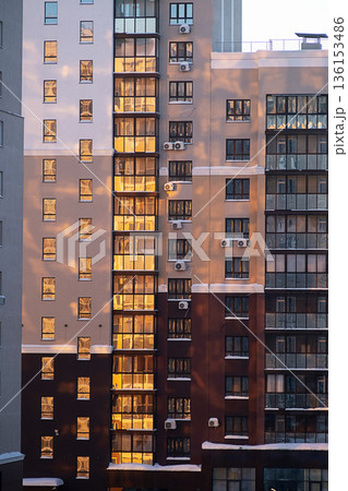 High rise apartment building facade with warm evening sunlight reflecting in many windows. High rise apartment building facade with warm evening sunlight reflecting in many windows. 136153486