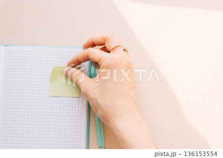 Hand placing sticky note on grid notebook, productivity and organization concept Hand placing sticky note on grid notebook, productivity and organization concept 136153554