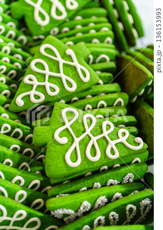 Captured from a close-up perspective, vibrant green Christmas tree-shaped sugar cookies with intricate white icing details are neatly arranged in stacks. The festive color and elegant piping design Captured from a close-up perspective, vibrant green Christmas tree-shaped sugar cookies with intricate white icing details are neatly arranged in stacks. The festive color and elegant piping design 136153993
