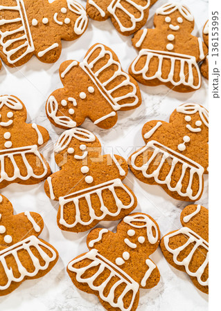 A large batch of gingerbread girl cookies featuring uniform royal icing designs, arranged to showcase the intricate dress and hair details. 136153995