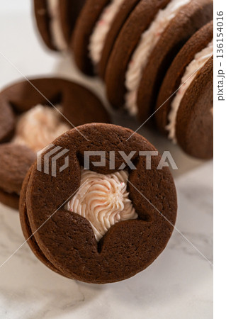 A single chocolate sandwich cookie shows a piped icing center through a star cutout. Minimal background and soft lighting emphasize shape and color. A single chocolate sandwich cookie shows a piped icing center through a star cutout. Minimal background and soft lighting emphasize shape and color. 136154016