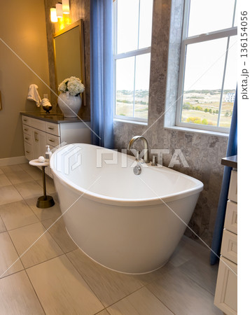 Elegant bathroom design featuring a freestanding white bathtub near a window with blue curtains. The neutral tones and natural daylight create a peaceful and refreshing look. The modern design Elegant bathroom design featuring a freestanding white bathtub near a window with blue curtains. The neutral tones and natural daylight create a peaceful and refreshing look. The modern design 136154056