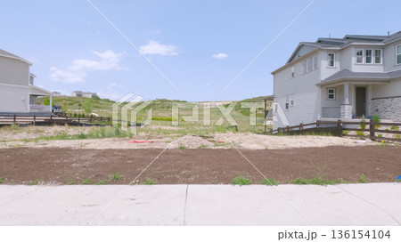 A backyard view in Castle Rock, Colorado showing patchy soil with an adjacent open green field. The surrounding homes are newly built with minimal landscaping. 136154104