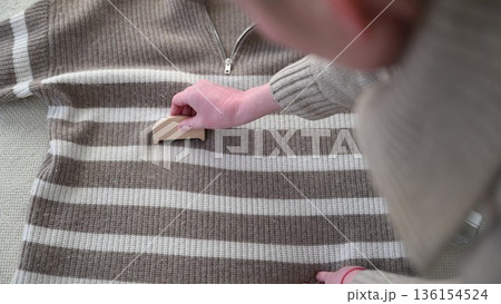 Woman removing lint from striped sweater with wooden fabric brush at home 136154524