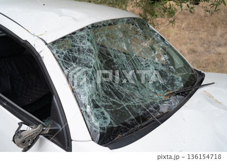 White car with a completely shattered windshield, broken glass, and damaged exterior after a serious road accident White car with a completely shattered windshield, broken glass, and damaged exterior after a serious road accident 136154718