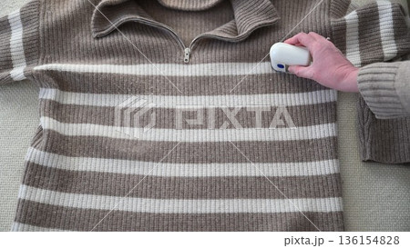 Woman using electric fabric shaver to remove pills from striped sweater at home 136154828