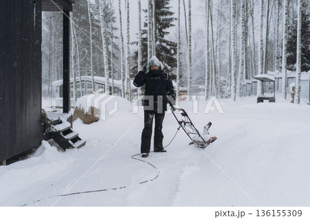 man clearing snowin countryside using electric snow blower 136155309
