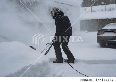 man clearing snowdrifts in countryside using electric snow blower 136155313