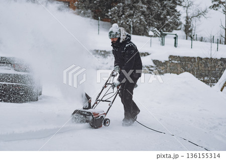 man clearing snowdrifts in countryside using electric snow blower 136155314