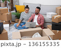 Home Happiness: A cheerful young couple, amid moving boxes in their new apartment, uses a laptop to shop for decor, create their dream space, or plan their move. 136155335