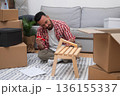 Self-Made Home: Young man constructs a DIY shelf in his new residence, surrounded by moving carton boxes, embracing the journey of relocating 136155337