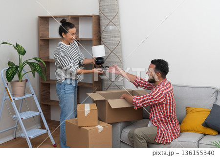 delighted young family, husband and wife, enjoys the process of moving into their new residence, placing a lamp on an empty shelf and embracing the joy of relocation 136155340