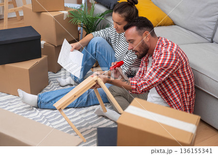 Young couple, boxes aplenty, construct modern wooden shelf furniture in their new apartment, enhancing their home's ambiance Young couple, boxes aplenty, construct modern wooden shelf furniture in their new apartment, enhancing their home's ambiance 136155341