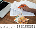 Close-up of a person calculating taxes with euros and tax forms on a wooden desk. Tax declaration and financial accounting concept  136155351