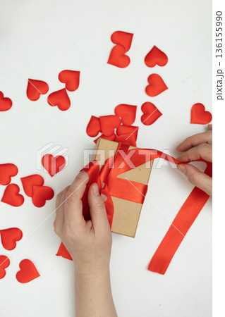Gift Wrapping for Valentine's Day With Red Ribbon and Heart Decorations on a White Table Gift Wrapping for Valentine's Day With Red Ribbon and Heart Decorations on a White Table 136155990