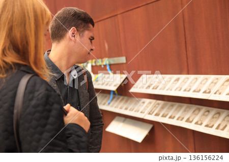 Man viewing memorial wall with portraits of fallen heroes, Ukraine ribbons. Silent tribute to fallen at portrait memorial display in Ukraine. Heavenly Hundred or Heavenly Company concept 136156224