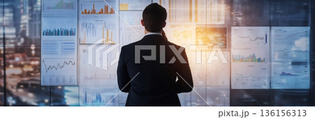 Businessman in a suit stands before a wall filled with charts and graphs, focusing on financial data analysis. The scene conveys multitasking, time management, and work stress 136156313