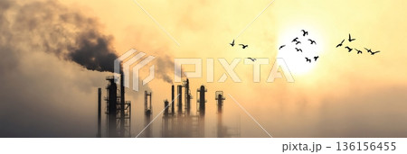 Petrochemical plant emitting dark smoke from industrial chimneys at sunset, filling the atmosphere with pollution while birds fly through a hazy sky tinged with orange 136156455