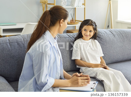 Child and counselor talking during therapy session on sofa in clinic setting 136157339