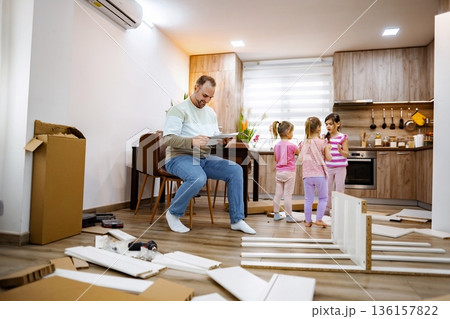 Father engages with children while assembling furniture in the kitchen Father engages with children while assembling furniture in the kitchen 136157822