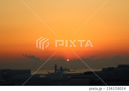 オレンジ色の空と朝陽とシルエットの雲と海と船と飛行機と空港の風景 136158024