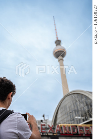 Berlin, germany, august 11, 2023. Person with backpack holding a smartphone, capturing a landmark structure and historic train station under a cloudy sky in berlin Berlin, germany, august 11, 2023. Person with backpack holding a smartphone, capturing a landmark structure and historic train station under a cloudy sky in berlin 136159527
