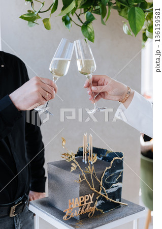 Couple clinking champagne glasses over luxury black and gold birthday cake, celebration moment 136159581