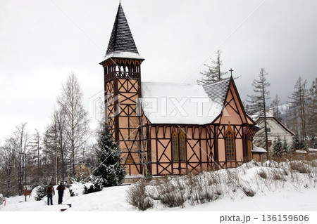 traditional half-timbered church with a tall wooden bell tower stands in a snowy winter landscape 136159606