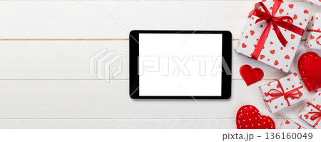 Digital tablet blank screen with gift box and hearts decor on wooden table. Top view. Valentines Day concept background 136160049