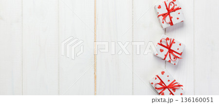 Valentine or other holiday handmade present in paper with red hearts and gifts box in holiday wrapper. Present box gift on white wooden table top view with copy space, empty space for design 136160051