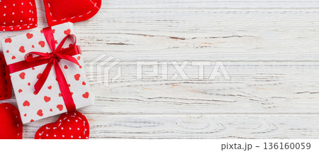 Valentine or other holiday handmade present in paper with red hearts and gifts box in holiday wrapper. Present box of gift on white wooden table top view with copy space, empty space for design Valentine or other holiday handmade present in paper with red hearts and gifts box in holiday wrapper. Present box of gift on white wooden table top view with copy space, empty space for design 136160059
